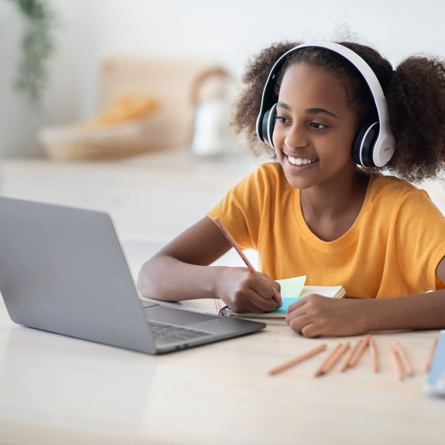 A girl with headphones on looking at her laptop.