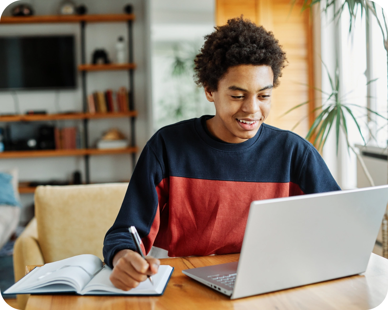 A young man is writing on his notebook while using a laptop.